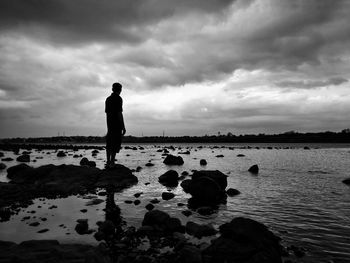Silhouette man standing on rock by lake against sky