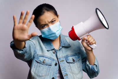 Close-up of young woman wearing flu mask holding megaphone against white background