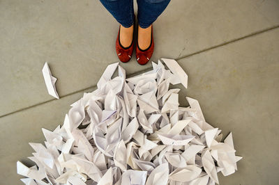 Low section of woman standing by white paper boats on floor