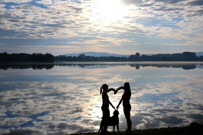 Silhouette friends on lake against sky during sunset