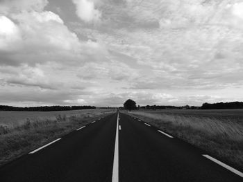 Empty road amidst field against sky