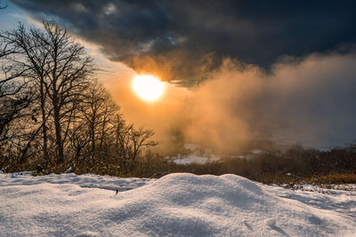 Snow covered field against sky during sunset