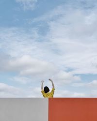 Rear view of woman with arms raised on building against sky