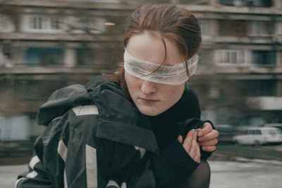 Close-up of woman with blindfold standing against building