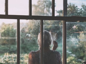 Rear view of smoking woman  through dusty window