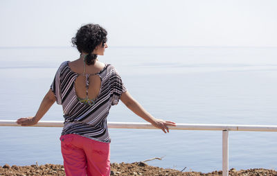 A woman is leaning on the railing and looking at the sea