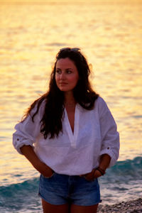 Portrait of smiling woman standing on sea during sunset