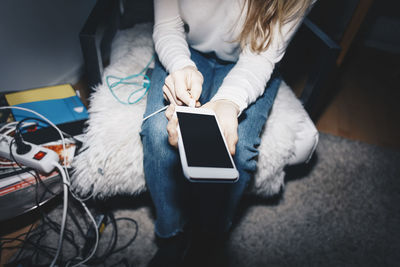 Midsection of woman plugging in mobile charging at college dorm room