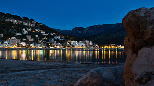 Illuminated buildings by sea against clear sky at night