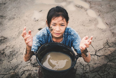 Portrait of girl holding muddy water in container on ground