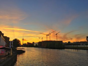 Silhouette city by river against sky during sunset