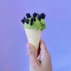 Cropped hand holding ice cream cone against blue background