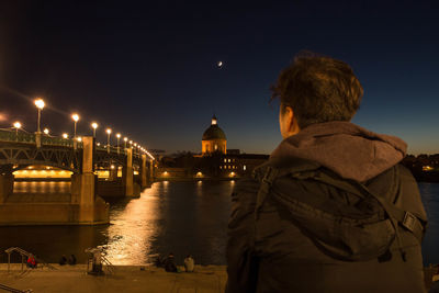 Rear view of woman standing by river against sky at night