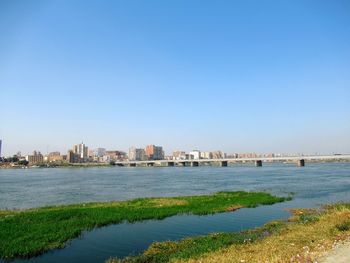 Scenic view of river by buildings against clear blue sky