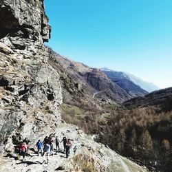 People on rocks against mountain range against clear sky