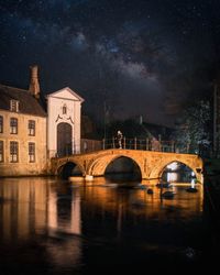 Arch bridge over river by buildings against sky at night