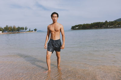 Full length of shirtless man standing at beach