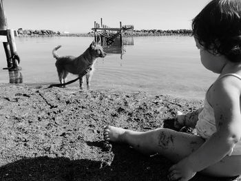 Little girl with dog on beach against sky