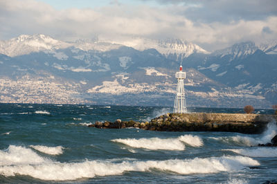 Lighthouse by sea against cloudy sky