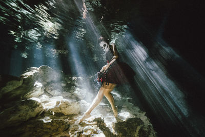 Full length of young woman standing on rock in forest