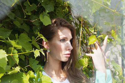 Portrait of young woman looking away against plants