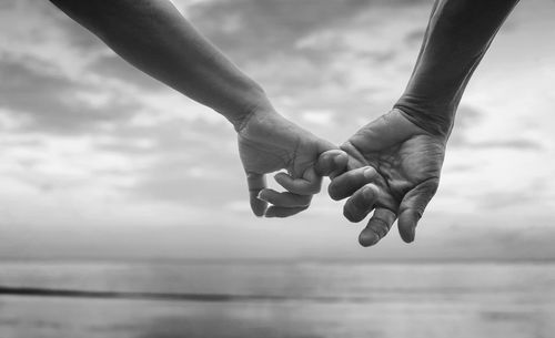 Cropped image of couple holding hands against sea at beach