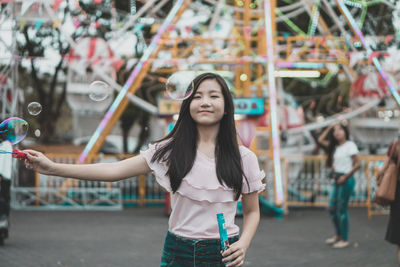 Portrait of young woman playing with bubbles at amusement park