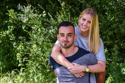 Portrait of happy young man piggybacking girlfriend at park