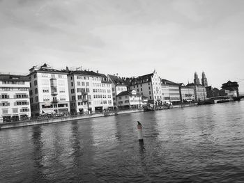 View of buildings by river against cloudy sky