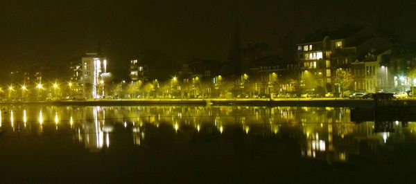 Illuminated city by river against sky at night