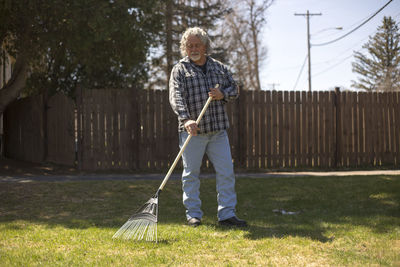 Full length of mature man raking in yard