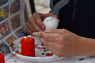 Midsection of man wax painting easter egg on table