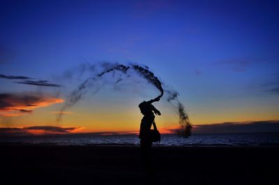 Silhouette man with smoke bomb standing at beach during sunset