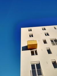 Low angle view of building with yellow balcony against clear blue sky