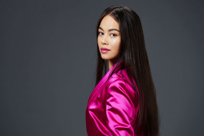 Portrait of young woman standing against gray background