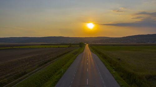 Road amidst field against sky during sunset