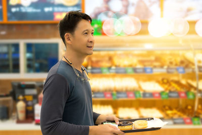 Side view of mid adult man holding donuts at store