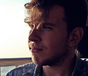 Close-up of thoughtful young man looking away sitting against sky