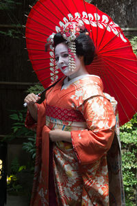 Woman wearing kimono holding red umbrella while standing outdoors