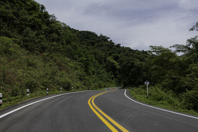 Empty road amidst trees against sky