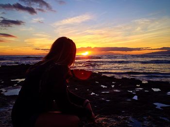 Woman looking at sea against sky during sunset