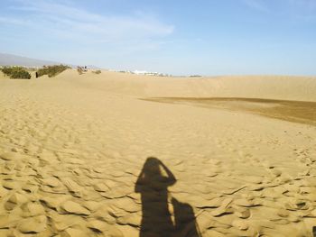 Shadow of man on sand in desert against sky