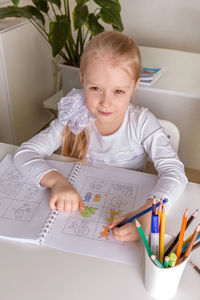 A girl student sits at a desk in the classroom and paints a picture with pencils. back to school 