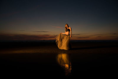 Woman standing on beach against sky during sunset