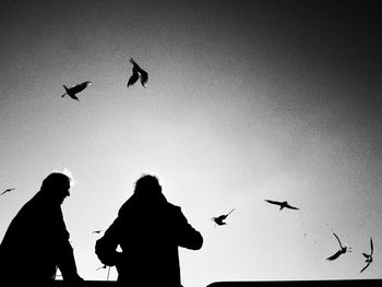 Low angle view of silhouette men flying against clear sky