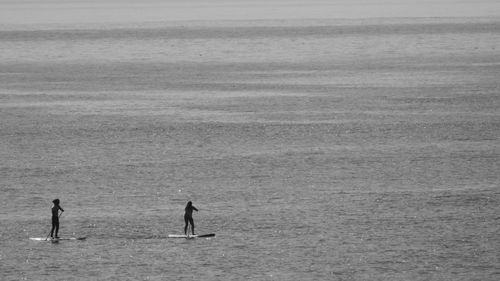 Full length of man and woman paddleboarding in sea