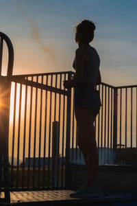 Rear view of silhouette man standing by railing against sky