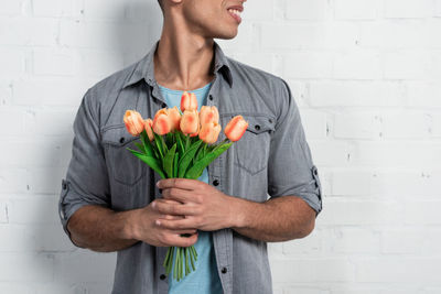 Midsection of man holding flower standing against wall