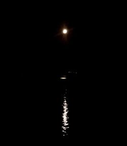 Reflection of illuminated moon in lake against sky at night