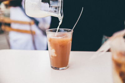 Milk pouring from jug into tea on table